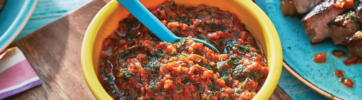 Yellow bowl of red chimichurri sauce on wooden board