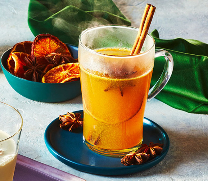 Tall clear heat-proof mug filled with hot buttered cider and a cinnamon stick garnish.