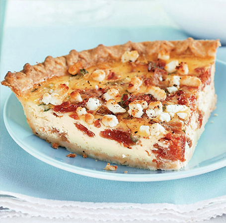 Quiche studded with bacon and tomato on pale-blue plate.