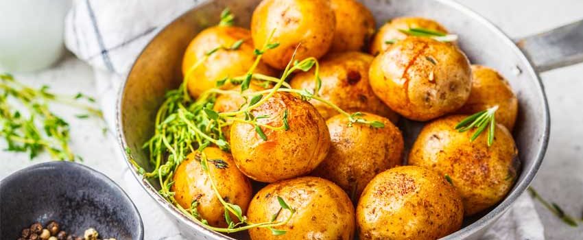 Potatoes in a gray bowl topped with fresh thyme and rosemary on a marble countertop.