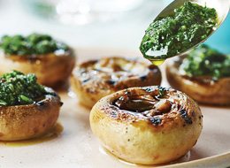 Close-up of mushroom caps filled with pesto sauce on a beige plate.