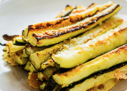 Zucchini sticks that have been grilled, piled on a plate, and seasoned with toasted breadcrumbs.