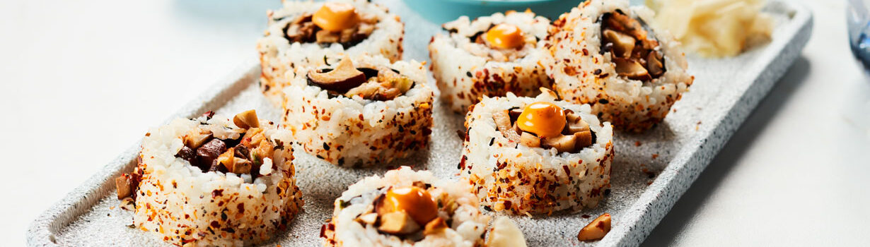 Several mushroom rolls sitting on a gray serving platter next to a little blue bowl of soy sauce.