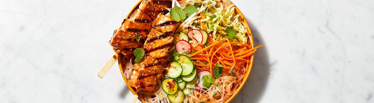 Orange plate topped with Teriyaki salmon skewer rice noodle salad.