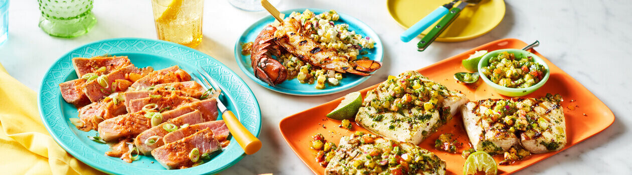 Grilled mahi-mahi filets, tuna steaks and lobster tails grilled, dressed and on various coloured plates.