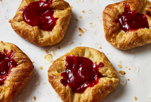 Baked danishes with red fruit filling on a parchment-lined baking sheet