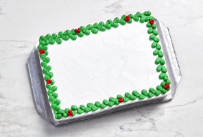 marble surface with rectangular white slab cake on silver sheet, with green and red holly buttercream edging and no centre decoration