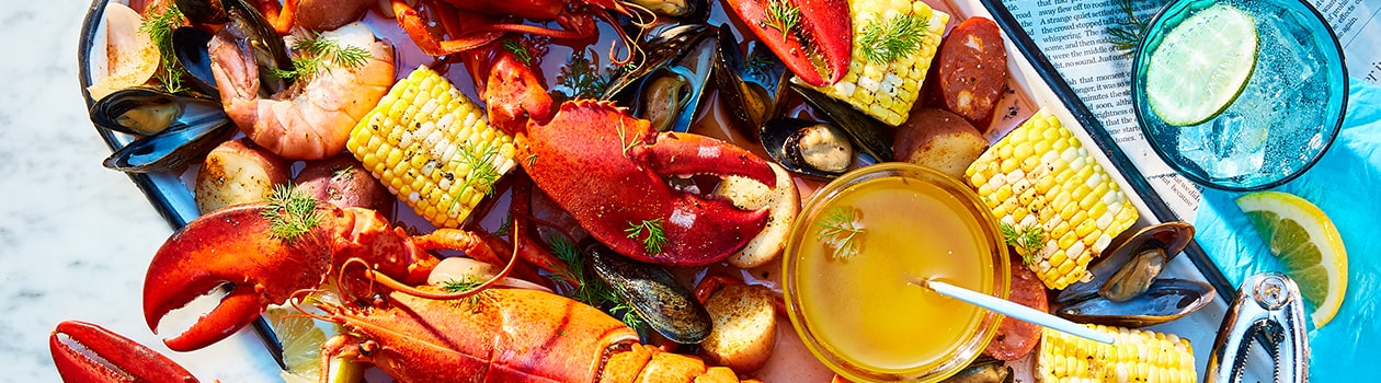 Platter filled with seafood boil of whole lobster, corn, mussels, shrimp, potatoes, and lemon.